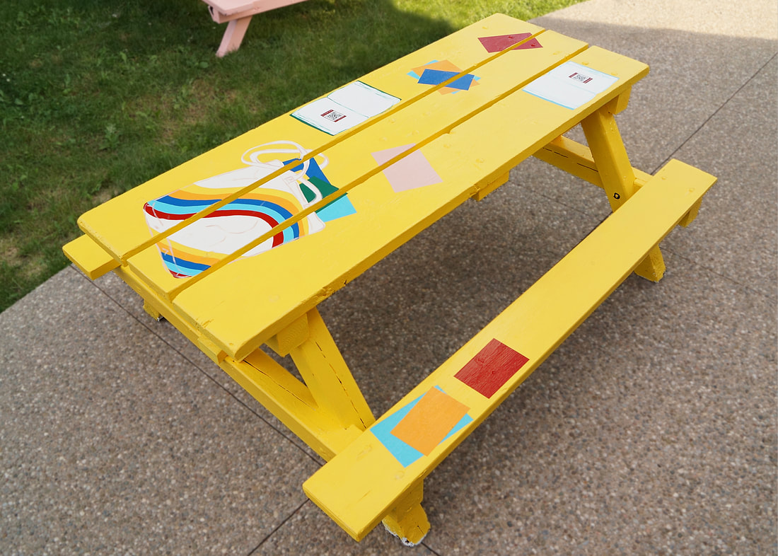 Picnic table painted to look like it's covered in books and a bag stuffed with books